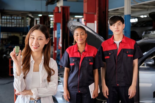 Young Asian female customer shows car key with automotive mechanic workers, happy smile in quality trust at maintenance garage, professional vehicle service center, fix check and repair auto industry. photo