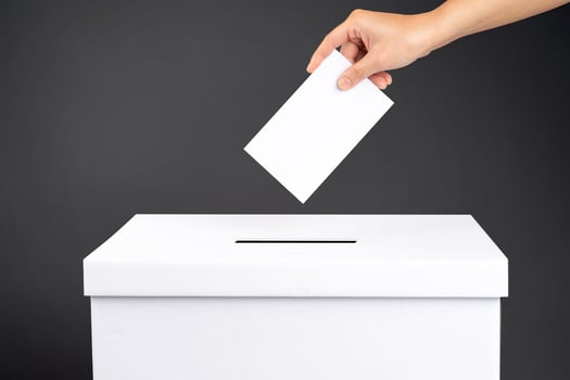 Female voter holds vote ballot paper in her hand above vote ballot for casting vote on black background photo