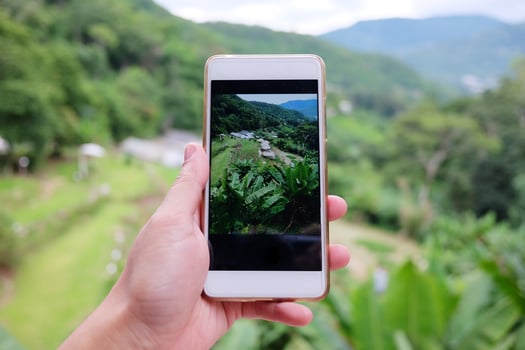 Woman hand holding smartphone for take a photo beautiful landscape valley mountain with Hill tribe village on green hill and forest in Rainy season at Thailand.