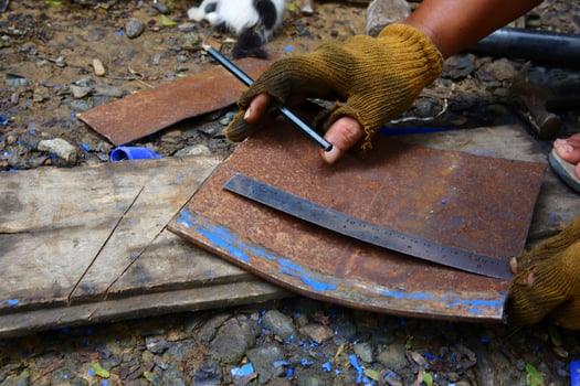 a hand is using a pencil and a ruler to measure the rusted iron to be cut photo