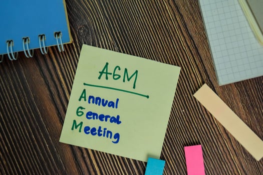 AGM - Annual General Meeting write on sticky notes isolated on Wooden Table. photo