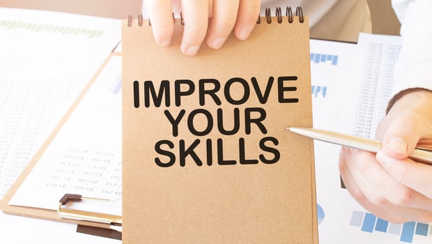 Text IMPROVE YOUR SKILLS on brown paper notepad in businessman hands on the table with diagram. Business concept photo