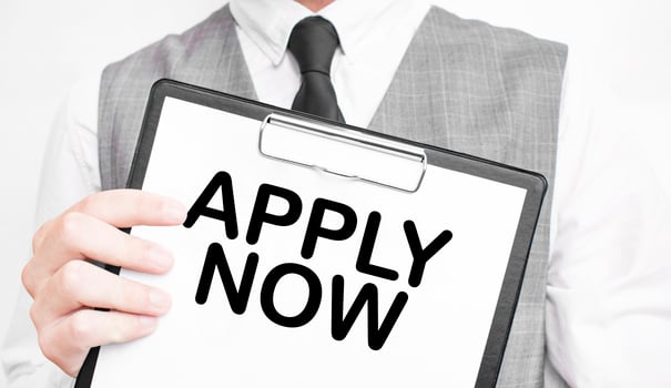 APPLY NOW inscription on a notebook in the hands of a businessman on a grey background, a man points with a finger to the text photo