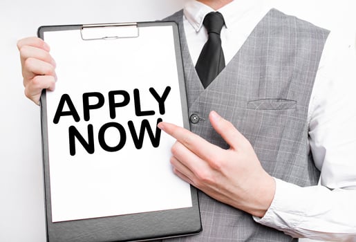 APPLY NOW inscription on a notebook in the hands of a businessman on a grey background, a man points with a finger to the text photo