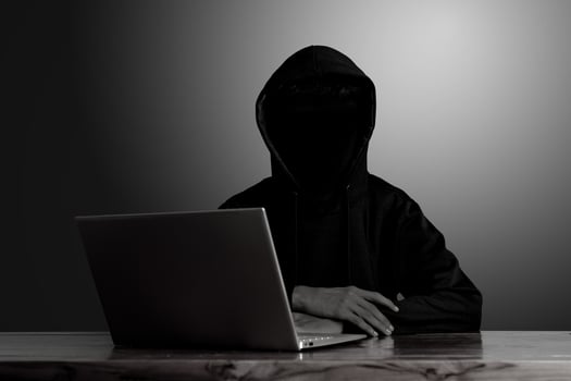 Mysterious man wearing black hoodie using laptop in the dark room. Hacker and cyber security concept. photo
