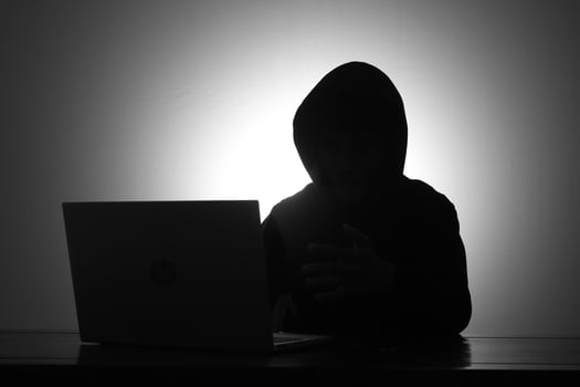 Mysterious man wearing black hoodie using laptop and holding credit card in the dark room. Hacker and cyber security concept. photo