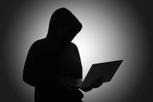 Mysterious man wearing black hoodie using laptop in the dark room. Hacker and cyber security concept. photo