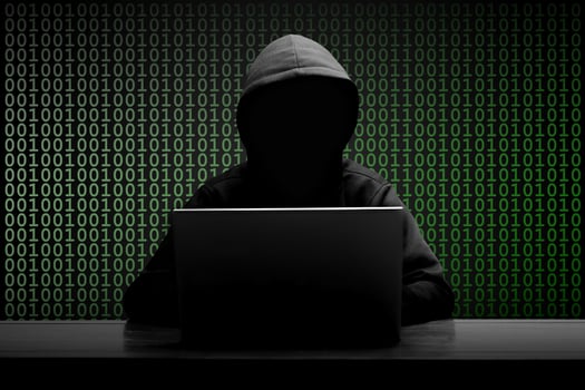 Mysterious man wearing black hoodie using laptop in the dark room. Hacker and cyber security concept. photo