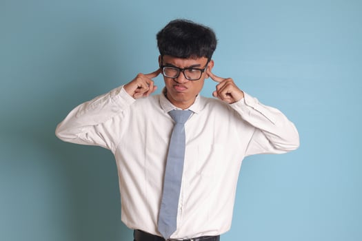 Indonesian senior high school student wearing white shirt uniform with gray tie covering his ears with his fingers, trying to avoid sounds or voices. Isolated image on blue background photo