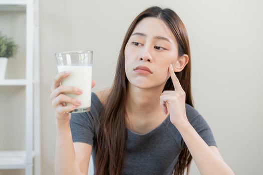 Allergy asian young woman, girl looking, holding glass of milk, face in thinking before drink milk as it may upset her stomach ache, pain. Lactose intolerance and dairy food , health problem concept. photo