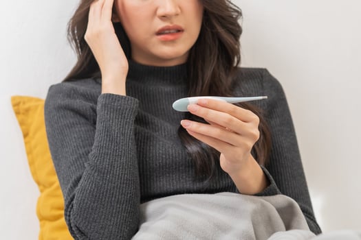Sick, influenza asian young woman, girl hand in using thermometer measure body temperature, have a fever, flu and feel illness sitting on sofa bed at home. Health care person on virus, covid-19. photo