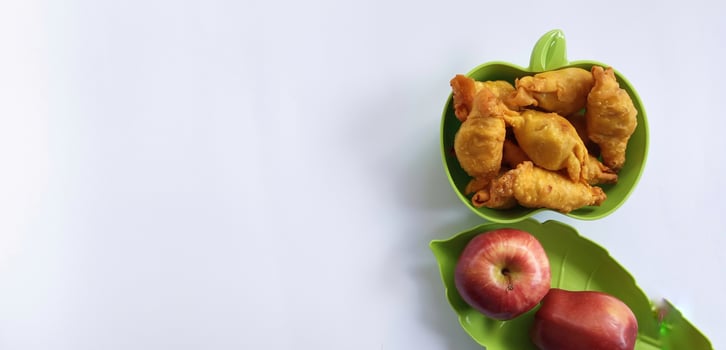 Fried sweet banana or pisang moleng in plate and red apple on white background with copy space. It is a typical Indonesian snack. Usually Sell at Street Food. photo