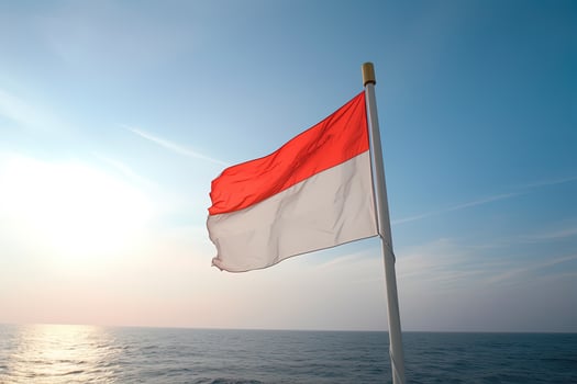 Indonesia national flag waving in the blue sky on the ocean background. Red and white flag with clouds. photo