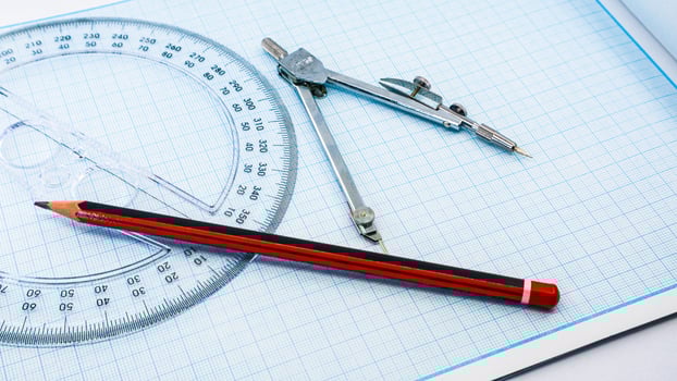 On blue graph paper are compasses, protractor, ruler, and a pencil photo