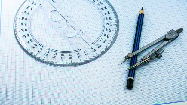 On blue graph paper are compasses, protractor, ruler, and a pencil photo