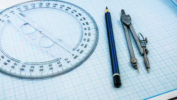 On blue graph paper are compasses, protractor, ruler, and a pencil photo
