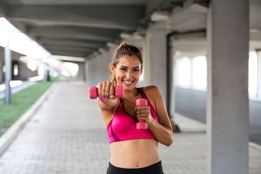 Sporty woman doing boxing exercises, making direct hit with dumbbells. Photo of muscular female wearing sportswear . Strength and motivation