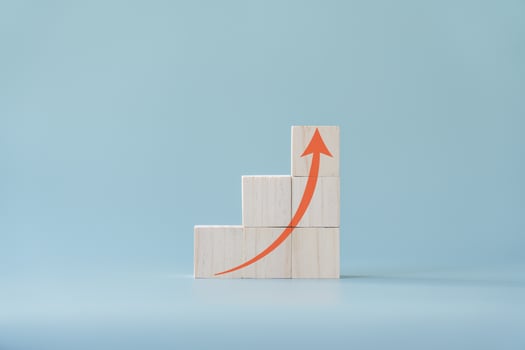 Red arrow going up on wooden blocks and light blue background. Concept of growing or improving. photo