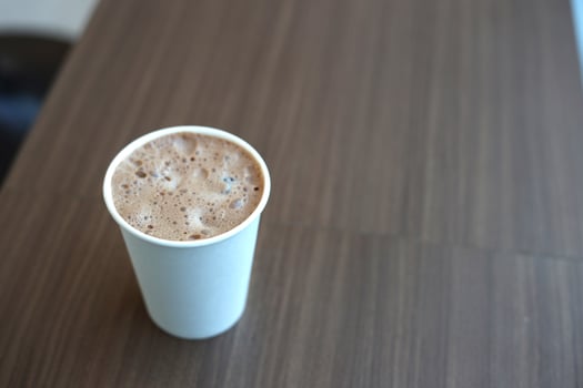 cocoa milk paper cup holding in woman hand with brown wooden table in cafe photo