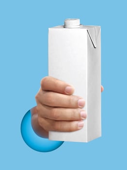 carton of milk or juice package in hand light blue background photo
