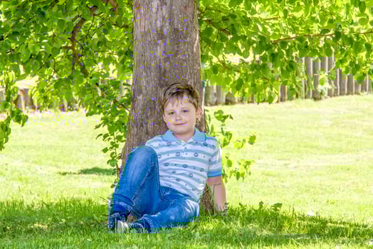 The boy is sitting in the shade under a tree. Hiding from the sun photo