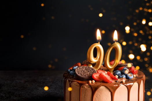 Chocolate birthday cake with berries, cookies and number ninety golden candles on black background, copy space photo