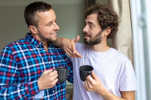 Young gay couple in love looking out the window. Two young androgynous men smiling together and having coffee. photo