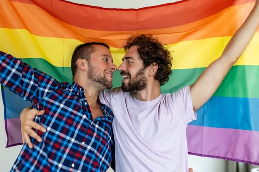 Two young gay lovers kissing each other affectionately. Two young male lovers standing together against a pride flag. Affectionate young gay couple sharing a romantic moment together. photo
