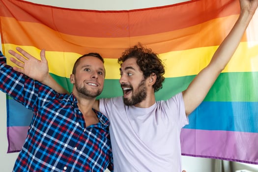 Two young gay lovers looking at each other affectionately. Two young male lovers standing together against a pride flag. Affectionate young gay couple sharing a romantic moment together. photo