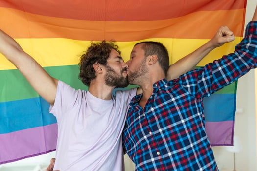 Two young gay lovers kissing each other affectionately. Two young male lovers standing together against a pride flag. Affectionate young gay couple sharing a romantic moment together. photo