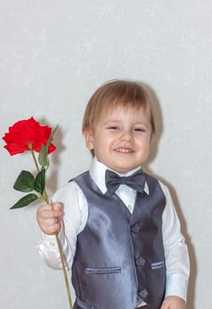 A little boy holds and hands over a red rose, the concept of the Valentine's Day theme. Portrait of a cute boy in a suit with a bow tie. photo