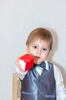 A little boy holds and hands over a red box, a Valentine's Day theme concept. Portrait of a cute boy in a suit with a bow tie. photo