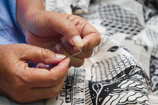 Close up photo of a woman's hands sewing batik cloth in Indonesia