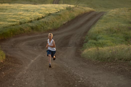 A boy in white t-shirt runs at sunset along a rural road next to a wheat field. Summer holidays in the countryside. Happy childhood photo