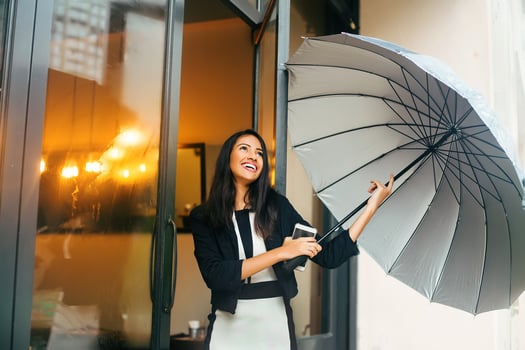 A beautiful young happy professional Indian woman wearing formals laughing with a phone and open umbrella in her hands photo