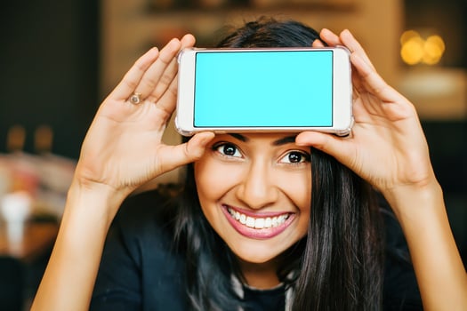 A smiling young Indian woman posing with her phone held to her forehead photo