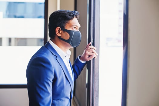 Indian young man wearing face mask and business suit looking from the window at home photo
