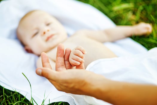 a baby laying on a blanket with a hand reaching out photo