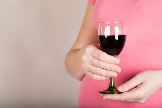 Young pregnant woman keeps a  glass of red wine. Closeup photo