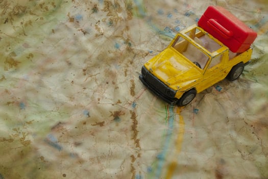 Mini car and a red plastic suitcase on a map. Closeup photo