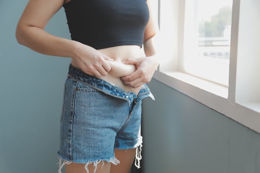 Close up of a belly with scar from c-section and abdominal fat. Women's health. A woman dressed up in sportswear demonstrating her imperfect body after a childbirth with nursery on the background. photo