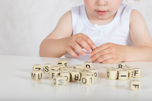 Small girl composes words from letters. Closeup photo