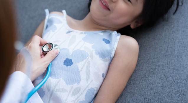 Asian woman pediatrician doctor hold stethoscope for exam a little girl patient and heck heart lungs of kid, Good family doctor visiting child at home, Healthcare and medicine for childhood concept. photo