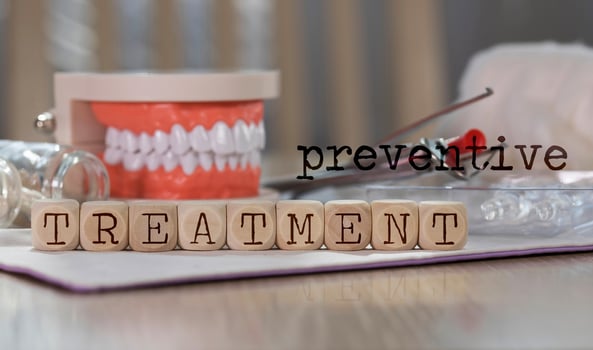 Words  PREVENTIVE TREATMENT composed of wooden dices. Pills, documents, pen, human jaw model in the background. photo