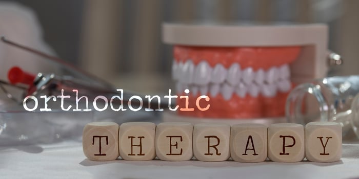 Words ORTHODONTIC THERAPY composed of wooden dices. Pills, documents, pen, human jaw model in the background. photo
