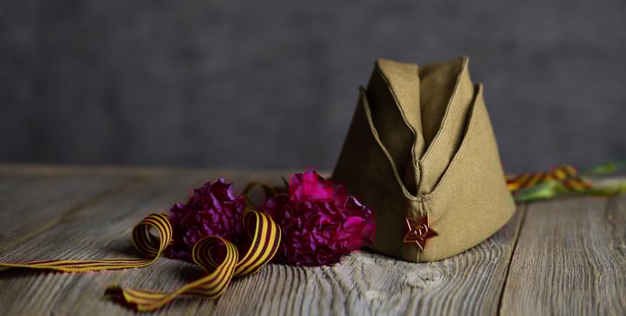 Military cap, carnations, Saint George ribbon on a wooden surface. photo