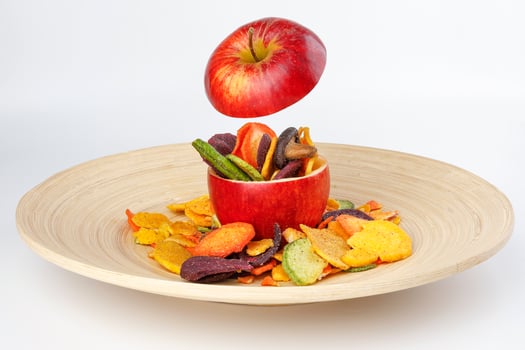 Healthy vegetable chips yellow sweet potato purple carrot green radish green beans and shiitake mushrooms in hollow red apple white background wooden plate photo
