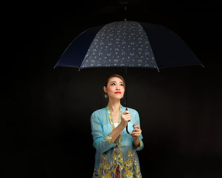 Asian woman in tractional kebaya carrying umbrella on black background photo