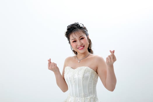 Young Asian woman in white dress hair done with crown on white background love finger sign photo