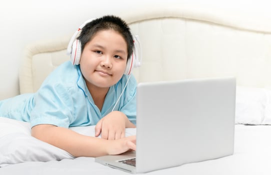 Obese schoolboy lying and wearing headphones to learn online from a laptop photo